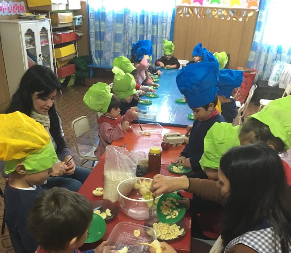 Estudiantes de nivel inicial con gorros de cocinero preparando una receta junto a sus docentes