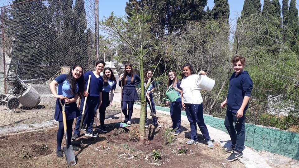 Estudiantes plantando y regando un árbol en la escuela